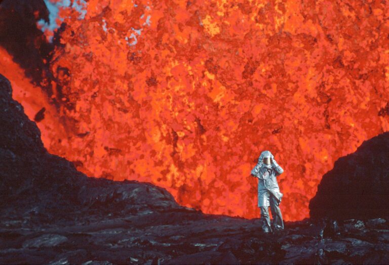 身着阻燃服的小人站在亮橙色的火山熔岩爆发前