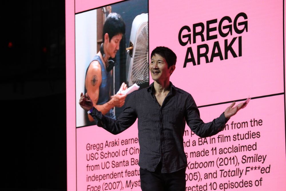 亚洲男人站在粉红色板前，上面写着“格雷格·阿拉基”，以及传记信息。