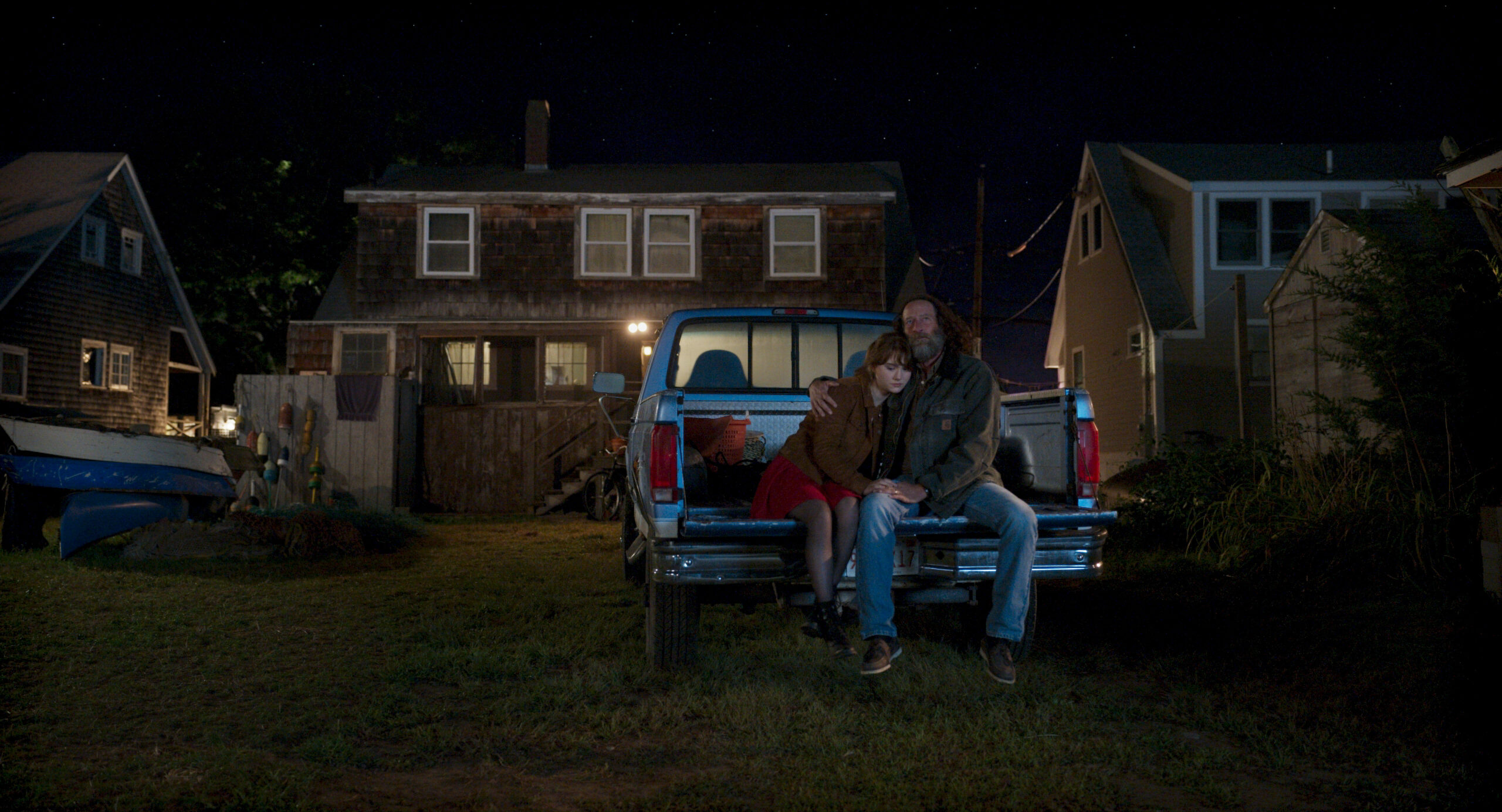 一个年轻的女人和一个年长的男人坐在一辆停在房子后面的小货车的后挡板上