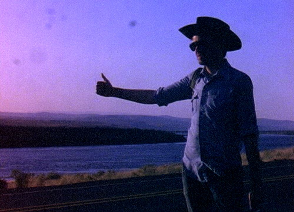 一个戴着牛仔帽的男人伸出大拇指在紫光中搭车。