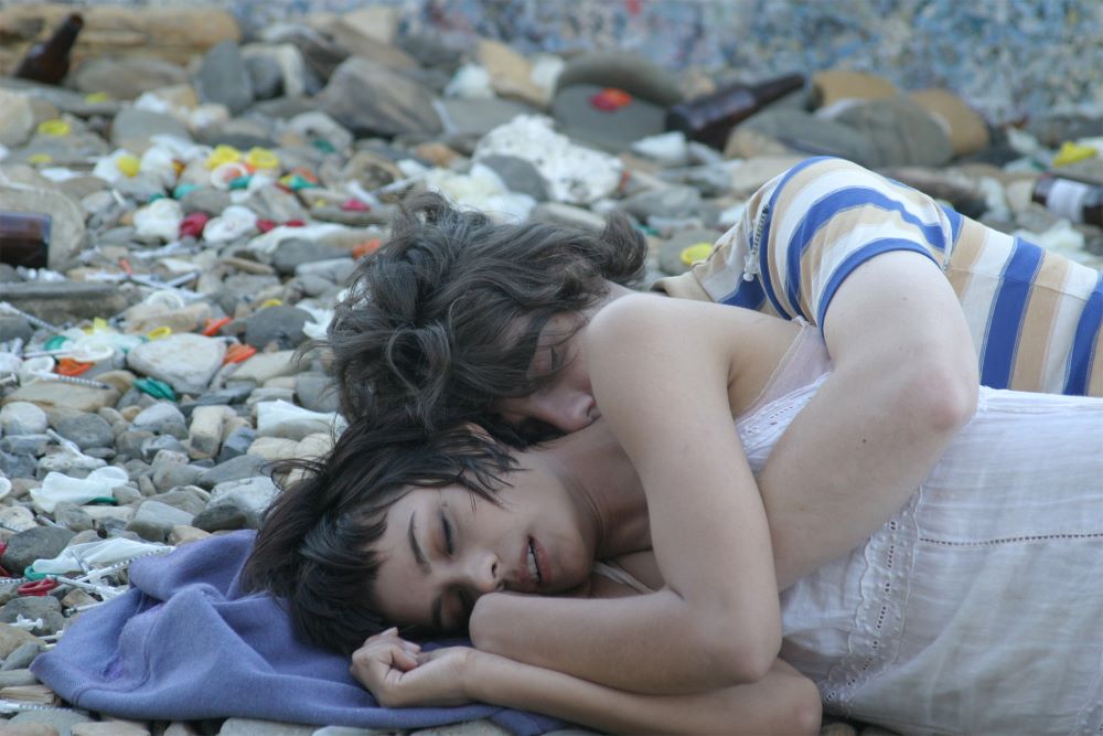 一个黑头发的年轻女人和一个黑头发的年轻男人躺在一条毯子上，躺在地上，彼此抱着枕头。