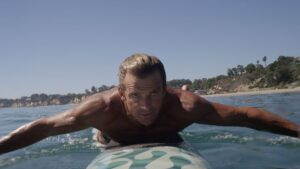 特写:一个男人躺在水中的冲浪板上，双臂向一侧划动