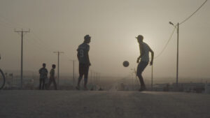 两个男人在街道中间踢足球，他们的身体呈剪影