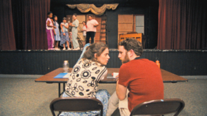 一个年轻女人棕色的头发谈判一个年轻人棕色的头发和一个橙色的衬衫。舞台的背景,剧院campgoers看着
