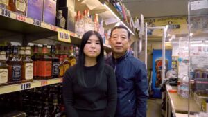年轻的亚洲女人和老亚洲男人站在货架上拿着酒瓶在商店里。