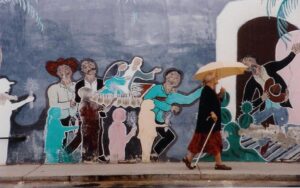 老女人与伞和一个拐杖走过一条色彩鲜艳的户外壁画。